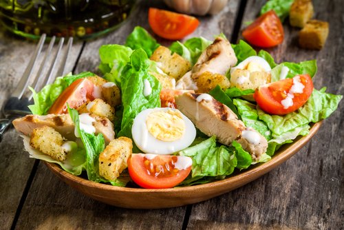 Caesar salad with croutons, quail eggs, cherry tomatoes and grilled chicken in wooden plate on dark rustic table